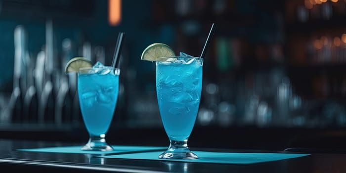 Two blue glasses with neon alcohol cocktails with lemons and ice on a bar counter