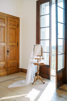 Bridal veil hangs on the mirror of the table near the open balcony door. High quality photo