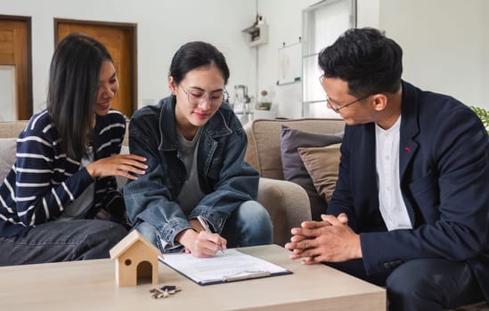 Asian couple looking at house plans and talking with a real estate agent about signing documents for purchase of a new home..