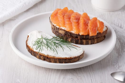 Rye sandwich with salmon and cream cheese on white wooden table.