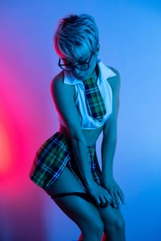 Sexy girl in an erotic school costume with a plaid skirt from sex shop takes off her underwear and panties in neon light