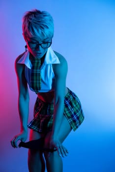 Sexy girl in an erotic school costume with a plaid skirt from sex shop takes off her underwear and panties in neon light