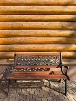 A wrought-iron bench stands next to a log building, Logs of a wooden house in close-up on a sunny day, a bathhouse, the hut. High quality photo