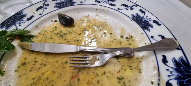 Close-up of an almost empty ornate plate after a seafood soup meal, with cutlery