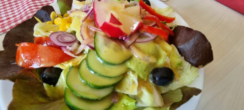 Close-up of a colorful and fresh mixed salad with lettuce, cucumbers, tomatoes, onions, olives, and corn, perfect for healthy eating and a delicious vegan or vegetarian appetizer, lunch, or dinner