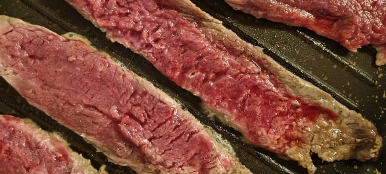 High-resolution image capturing succulent raw steak strips on a hot grill pan, ideal for food advertising