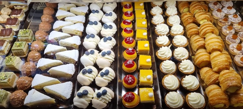 Close up display of assorted bakery delights including pastries, cakes, croissants, tarts, muffins, and confections at a gourmet patisserie for commercial food photography and indulgence