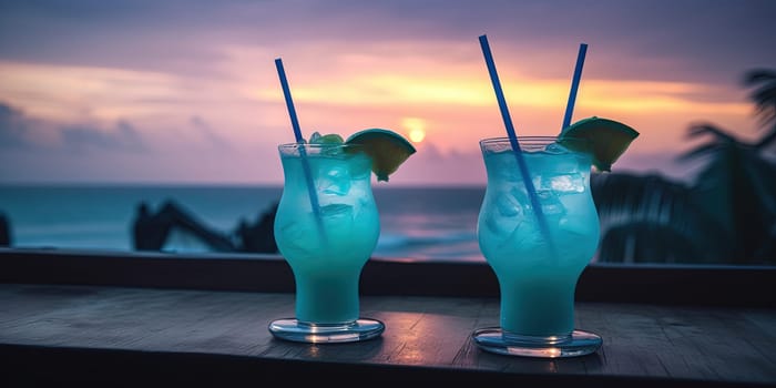 Two blue neon cocktails with alcohol, lemon and ice on a cafe table on a beach at sunset