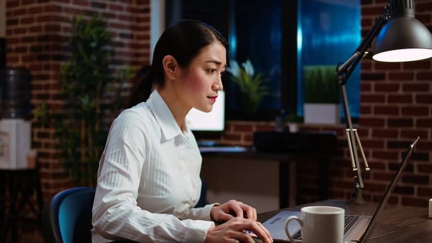 Businesswoman transcribing information from laptop to notepad, doing tasks for team project in office overnight. Worker working late at night, writing down data from computer screen