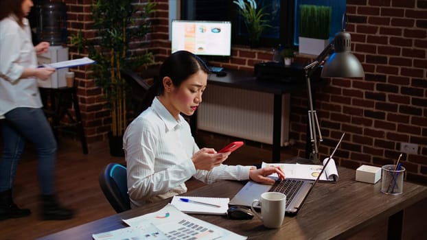 Stressed businesswoman doing multitasking, answering phone while crosschecking data between laptop and paperwork. Worker taking telephone call and comparing financial statistical graphs