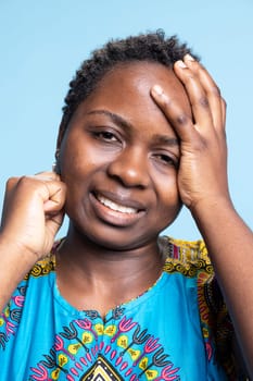 Sick person in traditional attire suffers from acute headache, having flu symptoms and feeling exhausted in studio. African american woman is struggling with serious pain in front of camera.