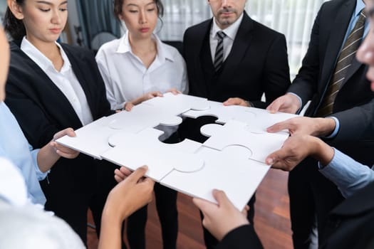 Multiethnic business people holding jigsaw pieces and merge them together as effective solution solving teamwork, shared vision and common goal combining diverse talent. Meticulous