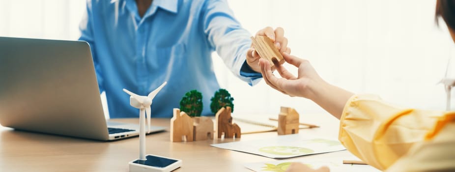 Two business people talking about eco city at green business meeting on meeting table with windmill represented renewable energy, wooden house block and tree model represent green city. Delineation.