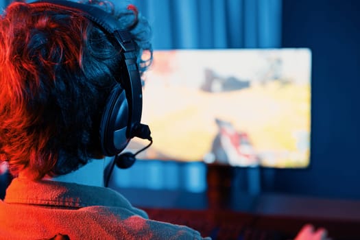 Host channel of young gaming streamer, team gamer playing battle game shooting with multiplayer at warship on pc screen with back side image, wearing headset with mic at digital neon room. Gusher.