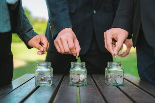 Business people put coin to money saving glass jar on outdoor table as sustainable money growth investment or eco-subsidize. Green corporate promot and invest in environmental awareness. Gyre