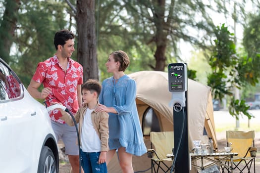 Outdoor adventure and family vacation camping in nature travel by eco friendly car for sustainable future. Lovely family recharge EV car with EV charging station in campsite. Perpetual