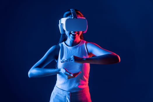 Smart Female standing surrounded by neon light wear VR headset connecting metaverse, futuristic cyberspace community technology, using both hands interact with generated virtual object. Hallucination.