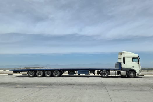 Side view of a large length cargo big truck with copy space on a blue sky.