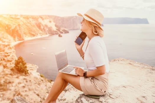 Digital nomad, Business woman working on laptop by the sea. Pretty lady typing on computer by the sea at sunset, makes a business transaction online from a distance. Freelance remote work on vacation