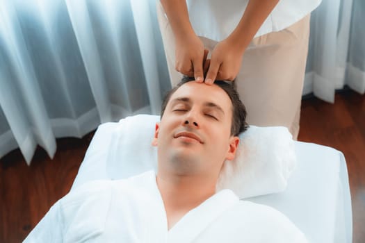 Caucasian man enjoying relaxing anti-stress head massage and pampering facial beauty skin recreation leisure in dayspa modern light ambient at luxury resort or hotel spa salon. Quiescent