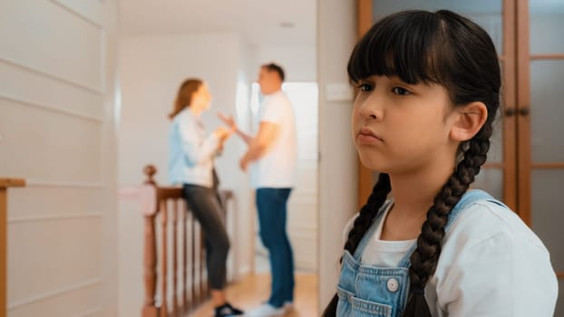 Stressed and unhappy young girl huddle in corner crying and sad while her parent arguing in background. Domestic violence at home and traumatic childhood develop to depression. Synchronos