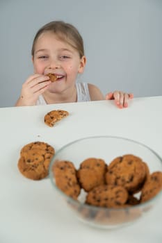 A little girl steals cookies from the table. Vertical photo