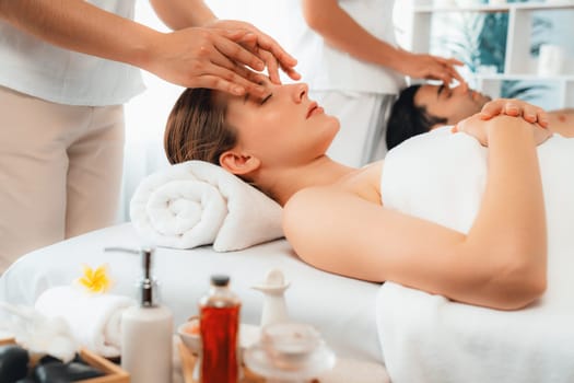 Caucasian couple enjoying relaxing anti-stress head massage and pampering facial beauty skin recreation leisure in dayspa modern light ambient at luxury resort or hotel spa salon. Quiescent