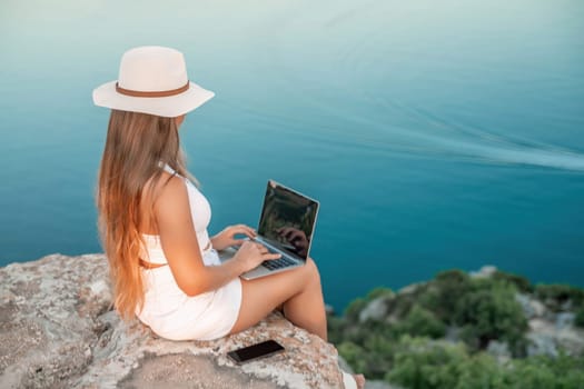 Freelance women sea working on the computer. Good looking middle aged woman typing on a laptop keyboard outdoors with a beautiful sea view. The concept of remote work