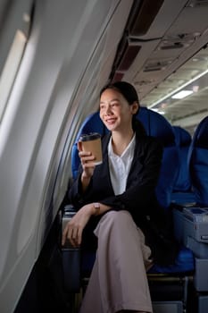 Young Asian woman sitting near the window on a business class airplane during a flight. Travel and business concept..