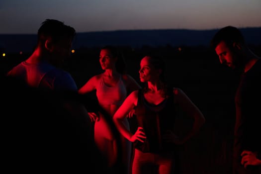 In the late-night hours, a diverse group of exhausted athletes find solace under a red glow, reflecting on their day-long marathon journey and celebrating camaraderie amidst fatigue.