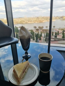 Paper cup of coffee and sandwich in a cafeteria on a glass table with a reflection of the sky.