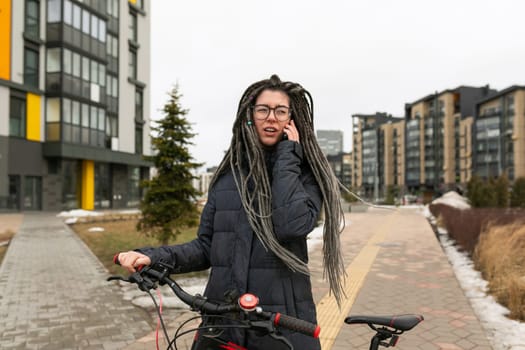 A pretty young woman with a dreadlocked hairstyle rides a bicycle and stops to rest.