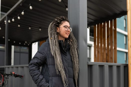 A pretty young woman with a dreadlocked hairstyle dressed in a winter jacket walks around the city.