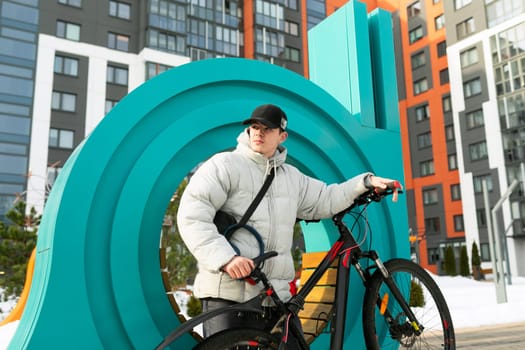 A young man in autumn clothes walks with a bicycle around the city.