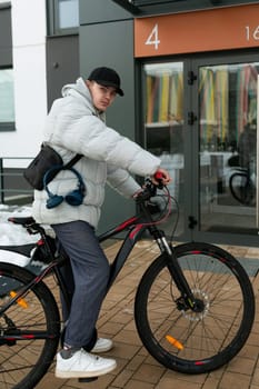 A young man in autumn clothes is waiting for a friend with a bicycle on the street.