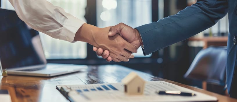 Two people shaking hands in front of a table with papers and a laptop by AI generated image.