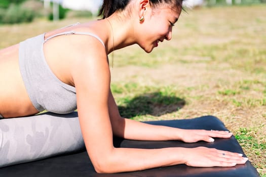 portrait of a young asian woman doing yoga exercises with her mat on the grass in the park , active and healthy lifestyle concept