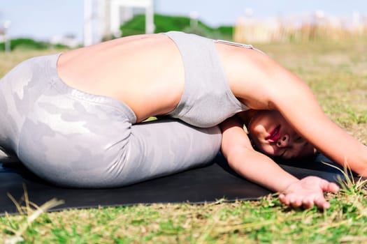 young asian woman doing yoga exercises with her mat on the grass in the park , active and healthy lifestyle concept