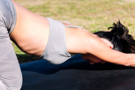 close up detail of an unrecognizable young woman doing stretching exercises with her yoga mat on the grass in the park, active and healthy lifestyle concept