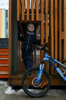 A European boy dressed in a winter jacket gets off his bike.