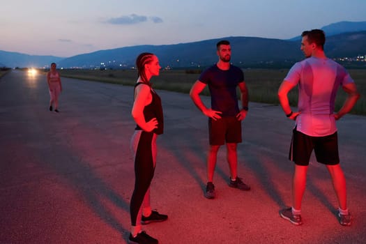 In the late-night hours, a diverse group of exhausted athletes find solace under a red glow, reflecting on their day-long marathon journey and celebrating camaraderie amidst fatigue.