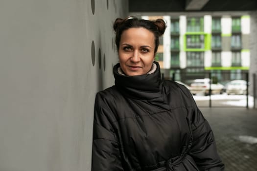 Weekend concept, portrait of a young brunette woman in a black jacket against a black wall.