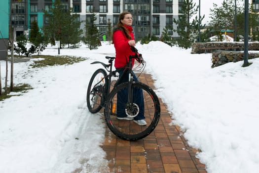 Cute young woman in a winter jacket rides a bicycle on the bike path.