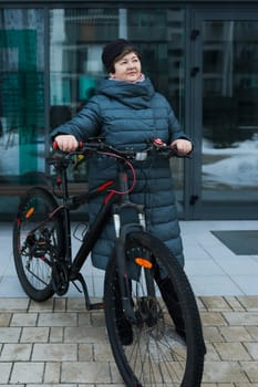 Mature European woman goes for a walk with a bicycle in winter.