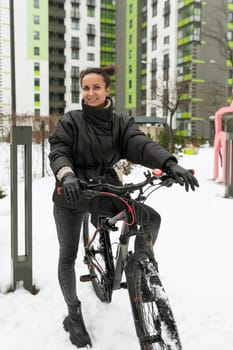 A young pretty woman in a winter jacket rented a bicycle and is riding it.