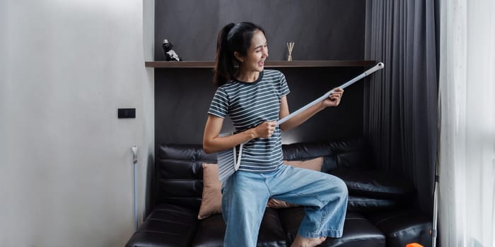 young asian woman having fun during cleaning, fooling with mop and broom.