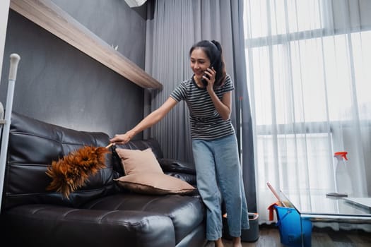 Young woman chit chat with friend on mobile while cleaning house on weekend.