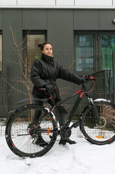 Sports concept, young woman with a bicycle walking around the city on a frosty day.