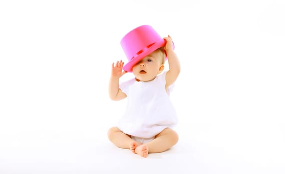 Happy cheerful baby playing with pink hat on the floor on white studio background