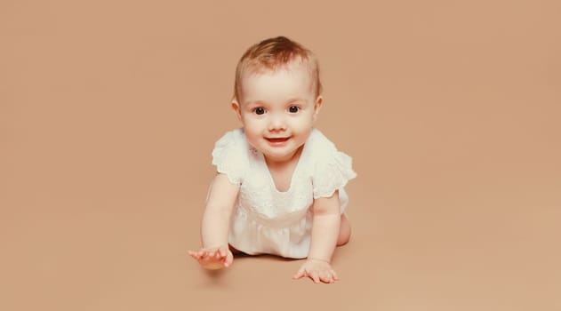 Portrait of happy cute baby crawling on the floor on brown studio background
